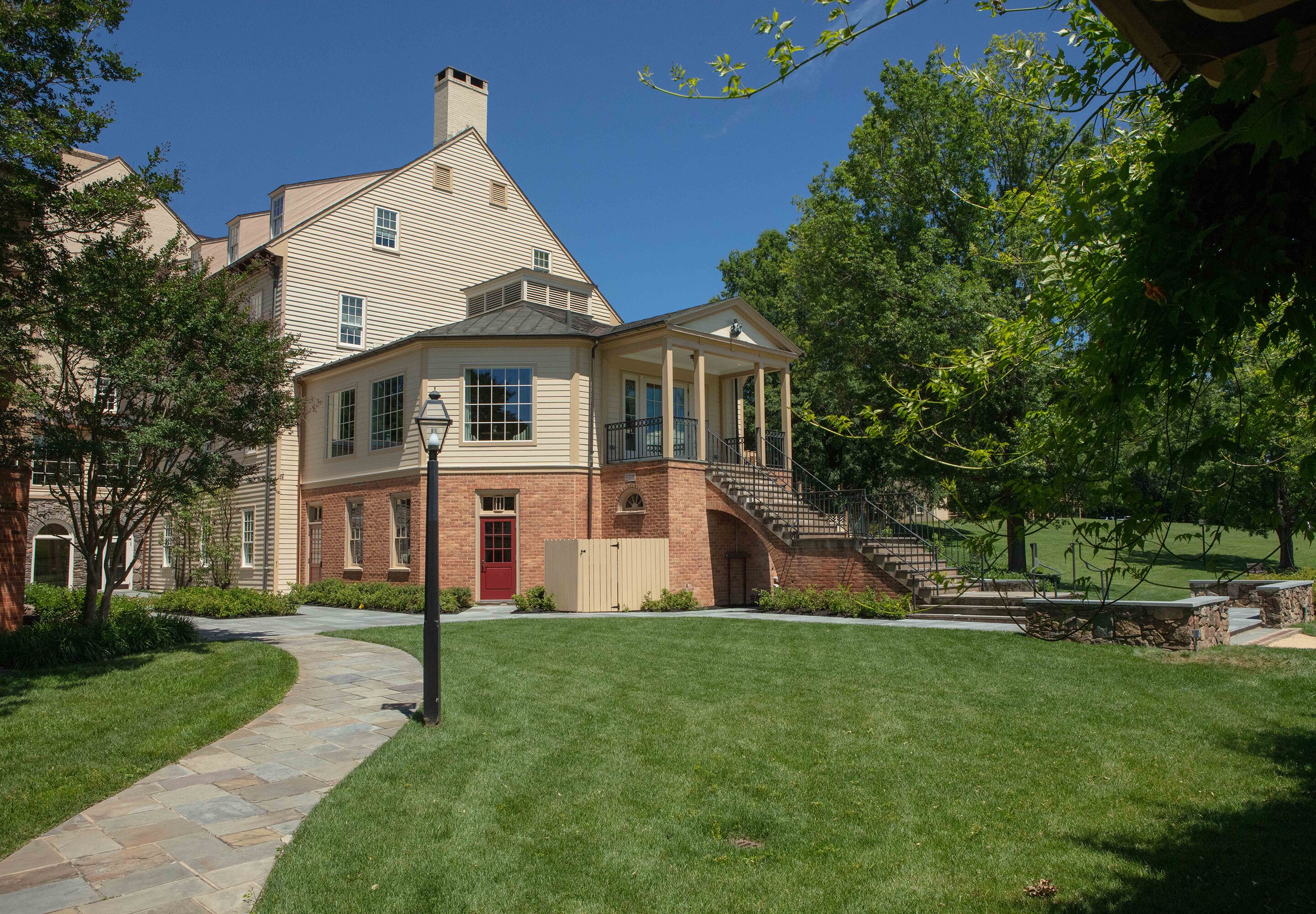 A two-story house with a brick facade, a red door, and a stone pathway leading to the entrance.