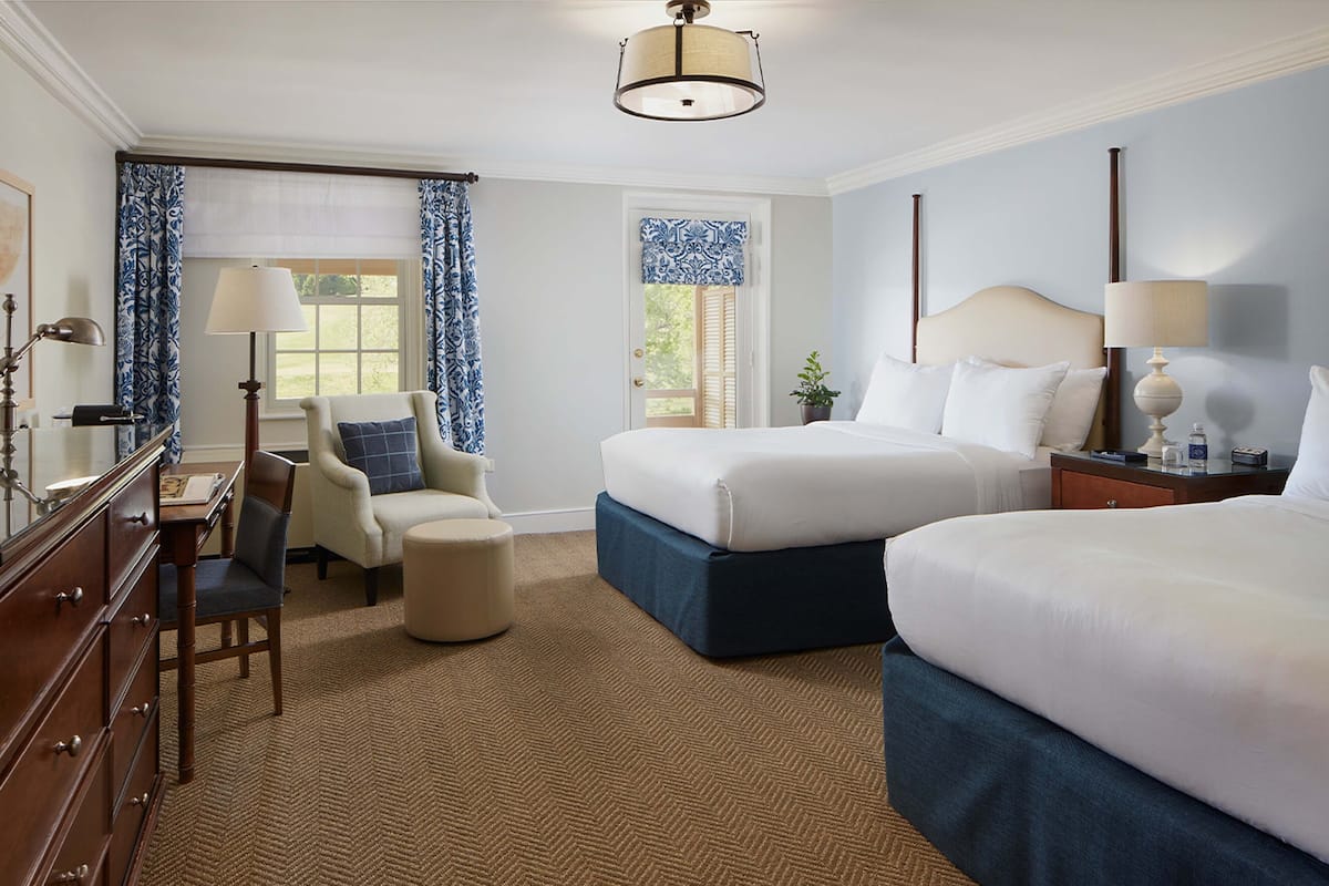 A hotel room with two beds, a desk with a chair, a dresser, and a window with curtains.