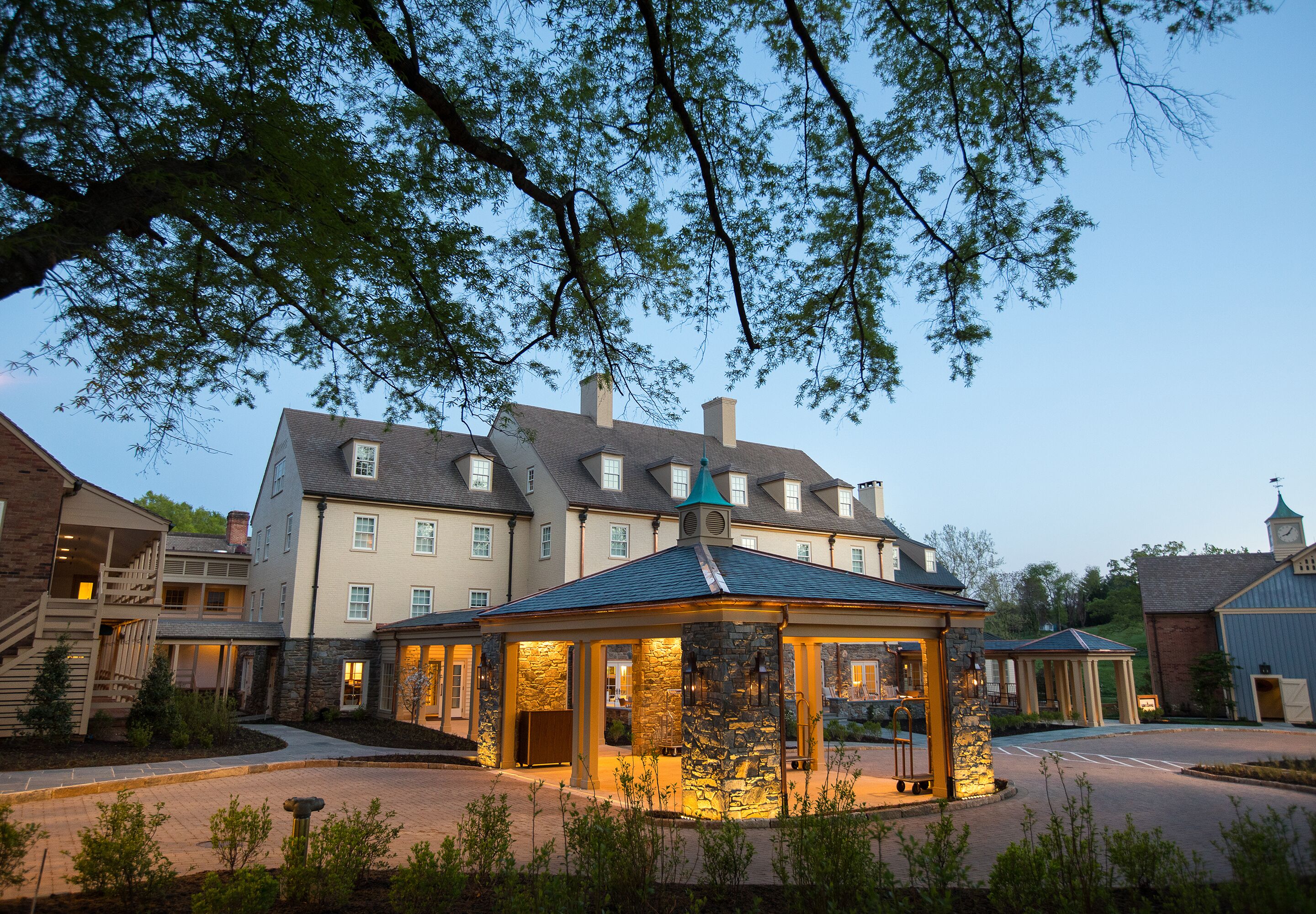 Een hotel met een gevel van natuursteen, een overdekt terras en een groot gebouw op de achtergrond.