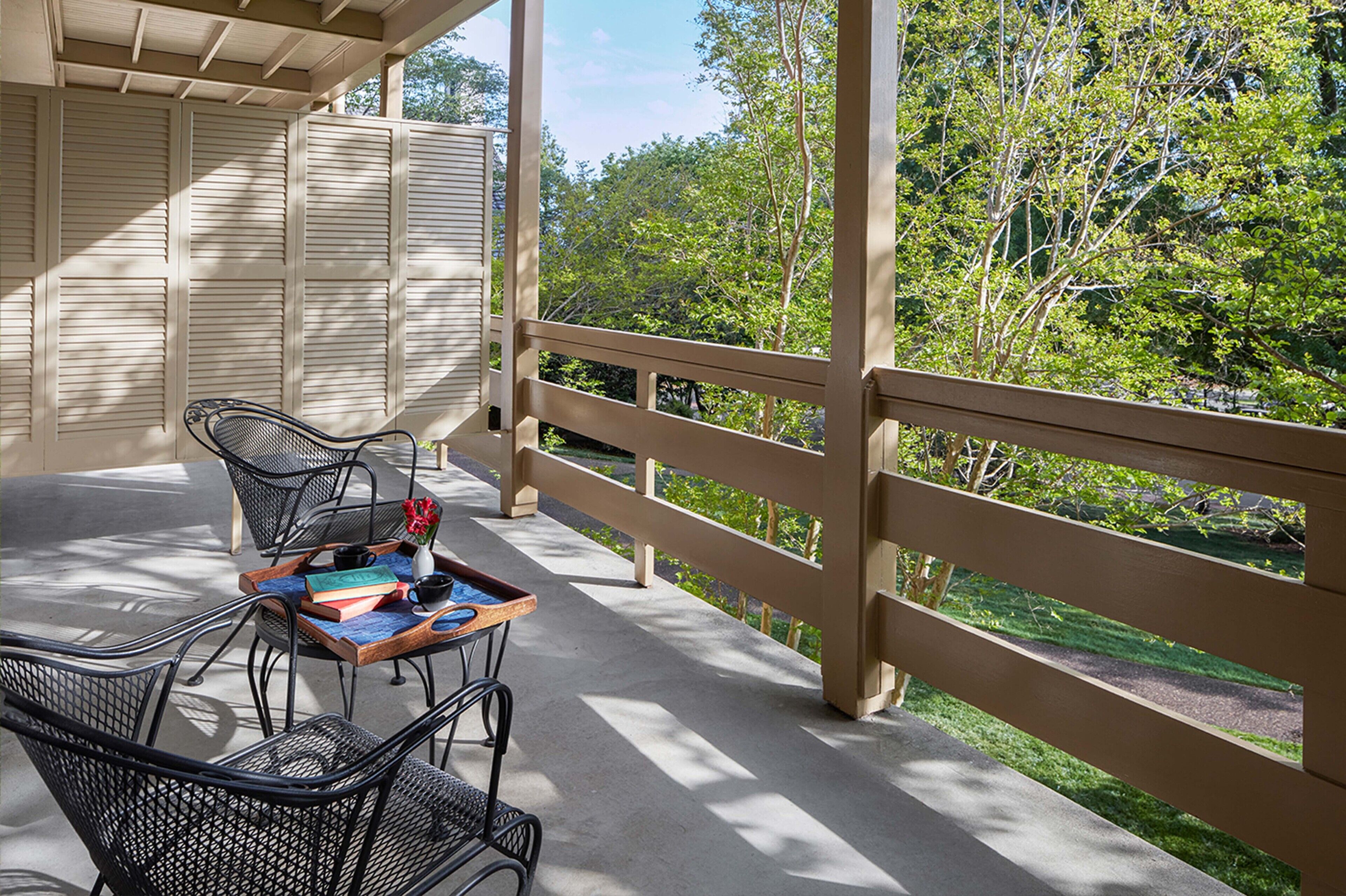 Un espace extérieur aménagé, abrité et doté de chaises en métal et d’une table, offrant une vue sur un jardin avec des arbres et un sentier.