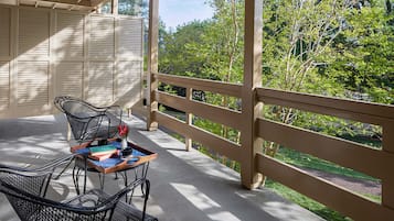 Un espace extérieur aménagé, abrité et doté de chaises en métal et d’une table, offrant une vue sur un jardin avec des arbres et un sentier.