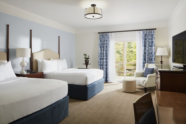 A hotel room with two beds, a desk, a chair, and a view of the outdoors.
