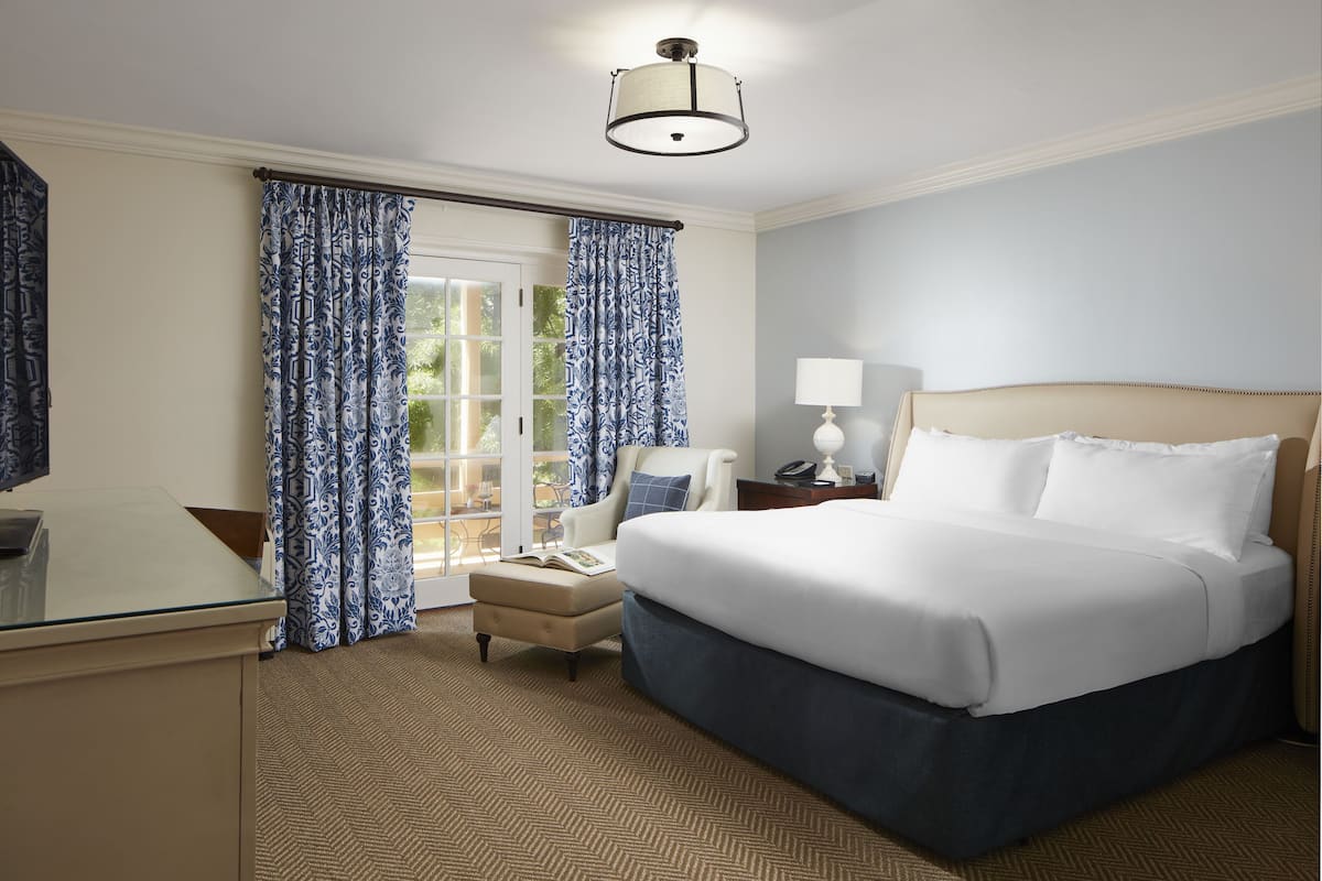 A hotel room with a large bed, a desk, a chair, and a lamp.
