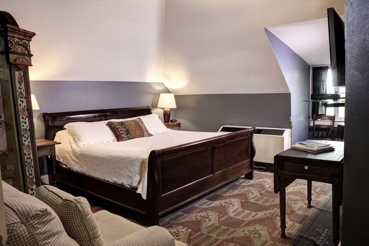A bedroom with a wooden bed, a bedside table, a lamp, a glass desk, and a chair.