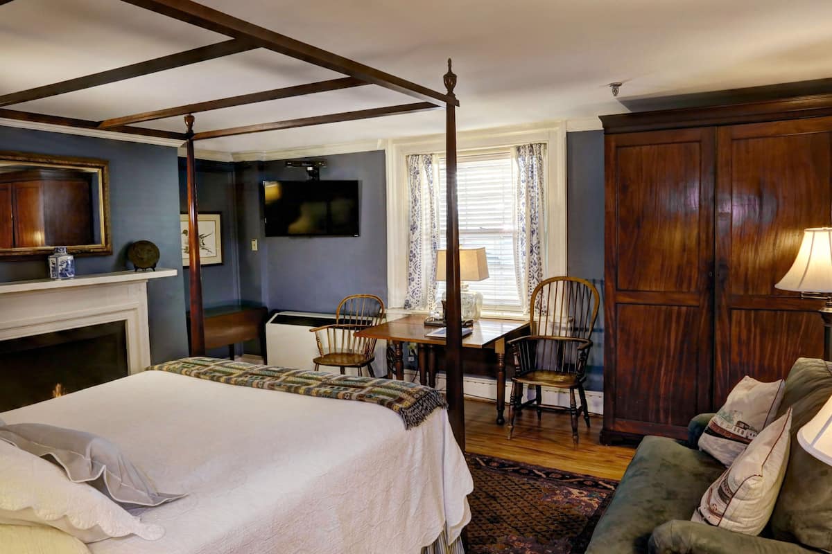 A four-poster bed, a wooden wardrobe, a television, a fireplace, and a dining table with chairs in a room with blue walls and wooden flooring.