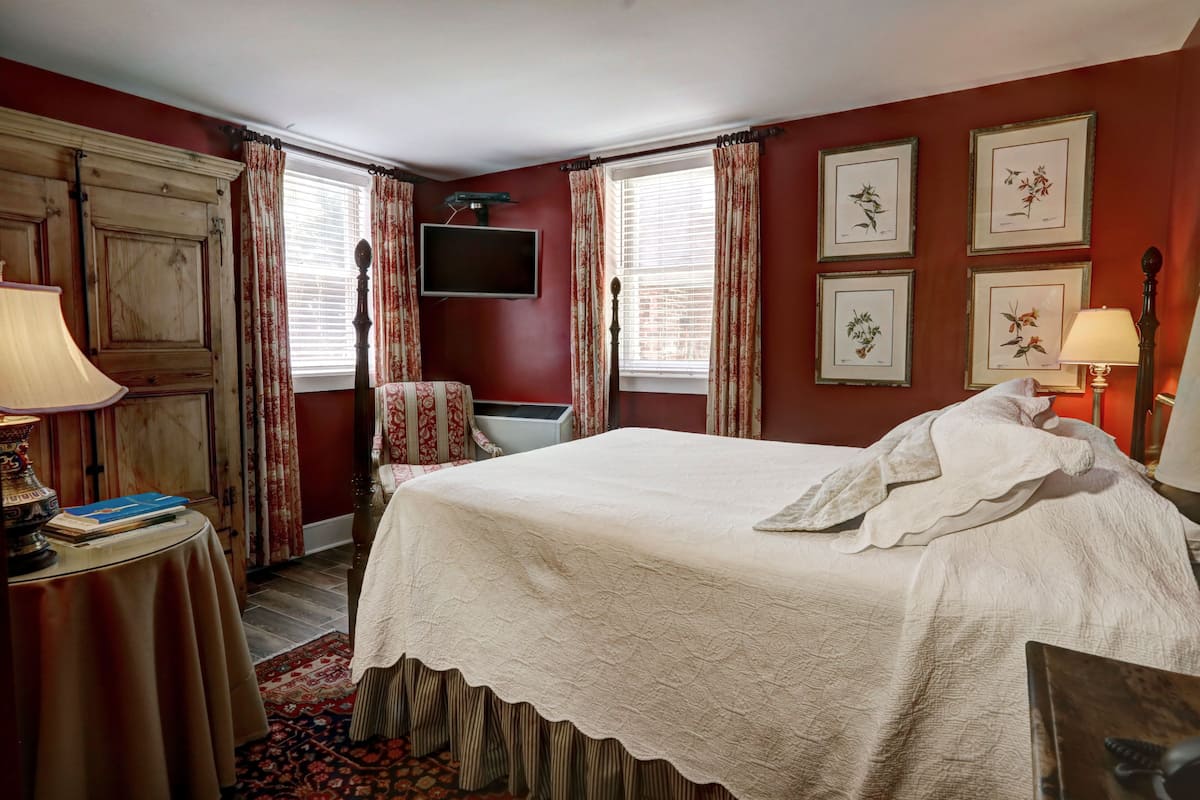 A bedroom with a large bed, a television mounted on the wall, and framed botanical prints on the wall.