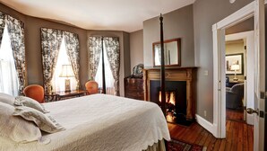 Ein Schlafzimmer mit Bett, Vorhängen, einem Kamin und einer Tür zu einem anderen Raum.