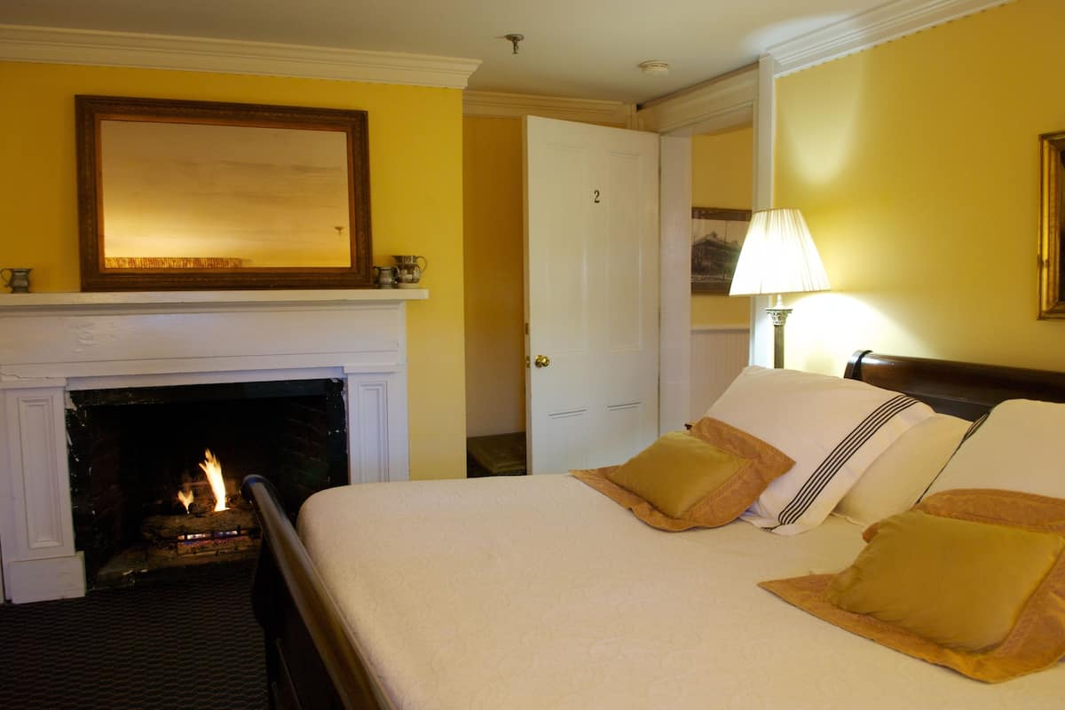 A hotel room with a fireplace, a bed with pillows, a lamp, and a door.