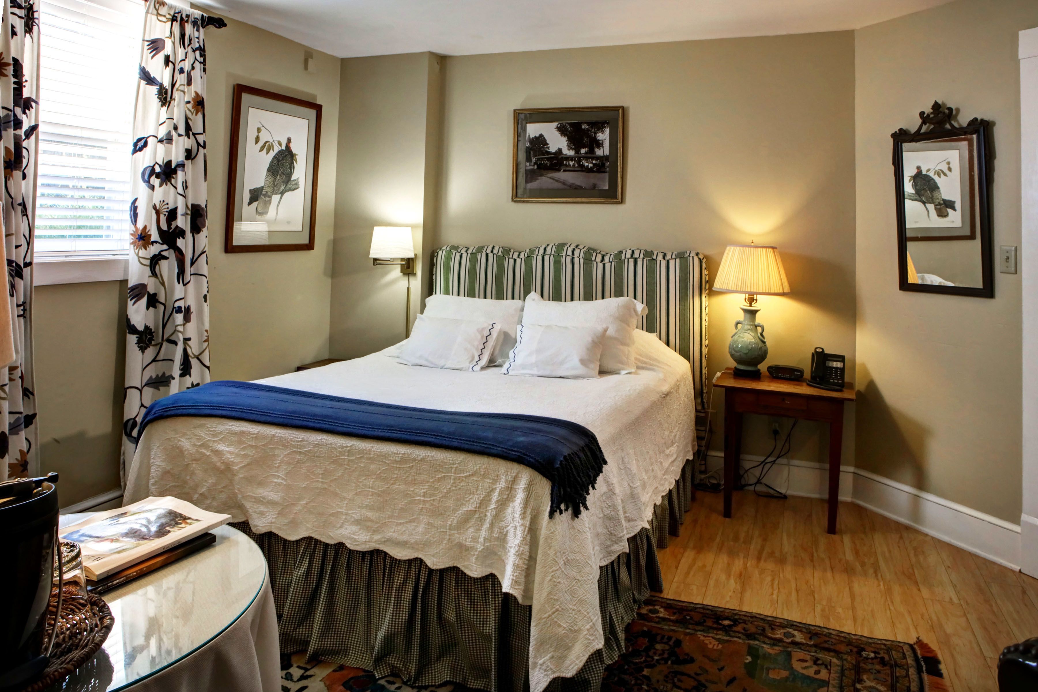A neatly arranged bedroom with a bed, bedside lamps, a small table, and a chair.