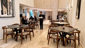 Un comedor moderno con mesas y sillas de madera, un camarero con uniforme y un interior limpio y bien iluminado.