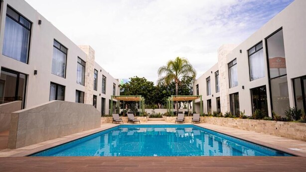 Un hotel moderno con piscina central, sillones de descanso y una zona de estar cubierta.