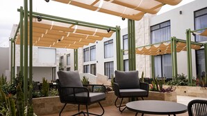 Un espacio de estar al aire libre con dos sillas y una mesa, rodeado de plantas y una estructura de pérgola.