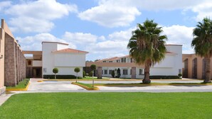 Un edificio moderno con un patio central, césped cuidado, palmeras y cielo despejado.