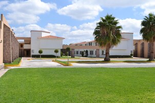Un edificio moderno con un patio central, césped cuidado, palmeras y cielo despejado.