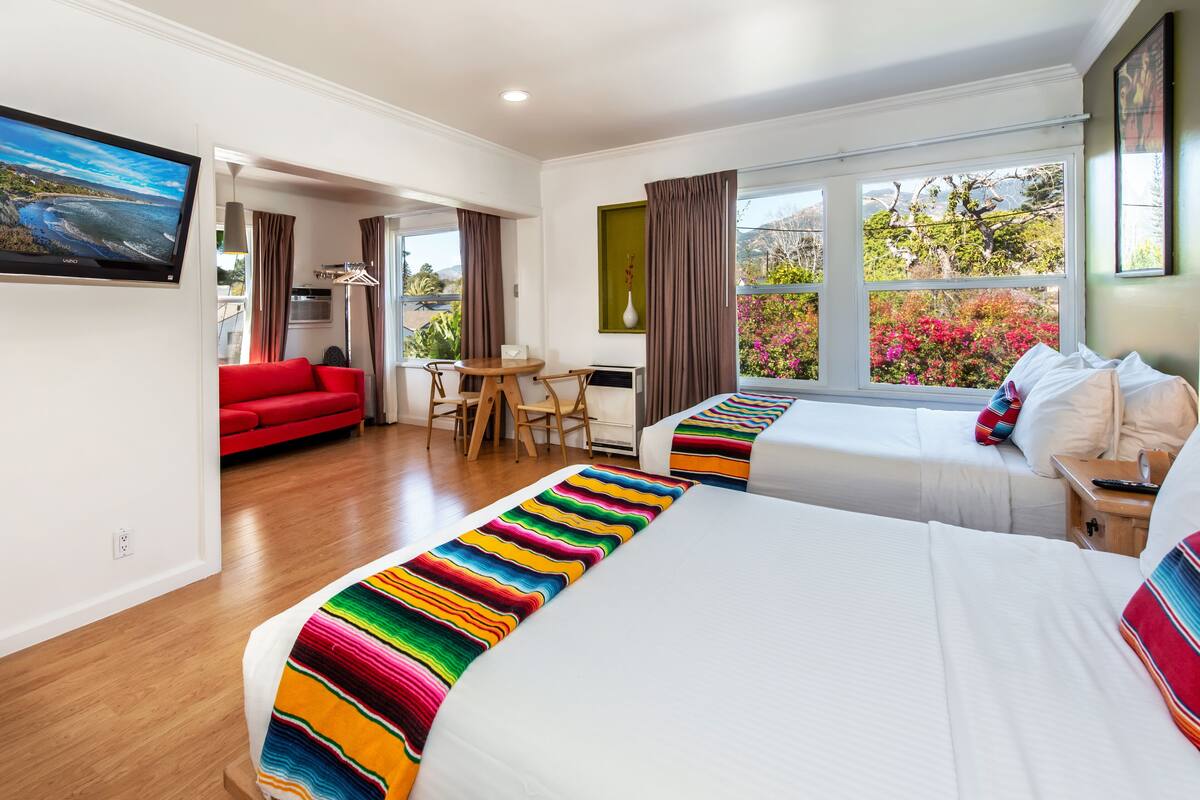 A hotel room with two beds, a red sofa, a dining table, and a TV.