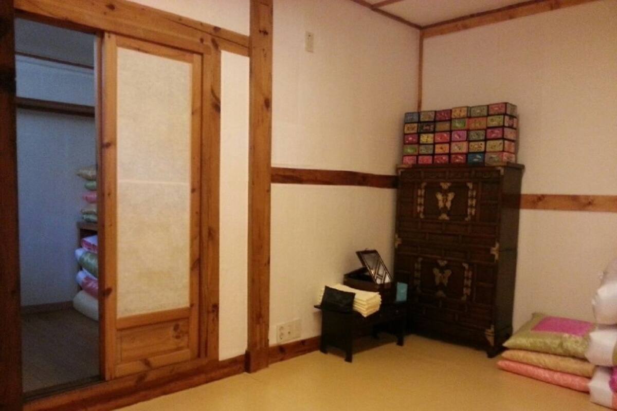 Une pièce de style japonais traditionnel, avec un sol recouvert de tatamis, une porte coulissante, un meuble en bois sombre et une petite table sur laquelle se trouve une lampe.