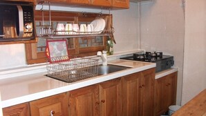 A kitchen with wooden cabinets, a microwave, a dish rack, and a stove. - Hyosunjae Hanok Guesthouse (Seoul)