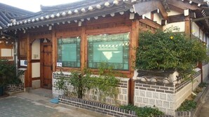 A traditional Japanese building with wooden architecture, a tiled roof, and a small garden area with plants and a brick wall. - Hyosunjae Hanok Guesthouse (Seoul)