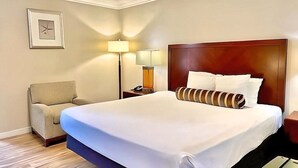 Hotellihuone, jossa on suuri sänky, tuoli, yöpöytä lampun kanssa ja seinällä oleva kehystetty kuva.