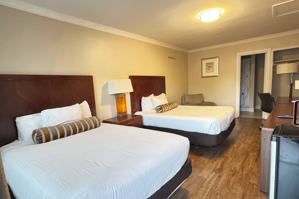 A hotel room with two beds, wooden headboards, a desk, and a chair.