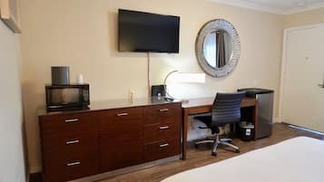 A hotel room with a bed, a desk with a computer, a chair, a television, a microwave, and a dresser.
