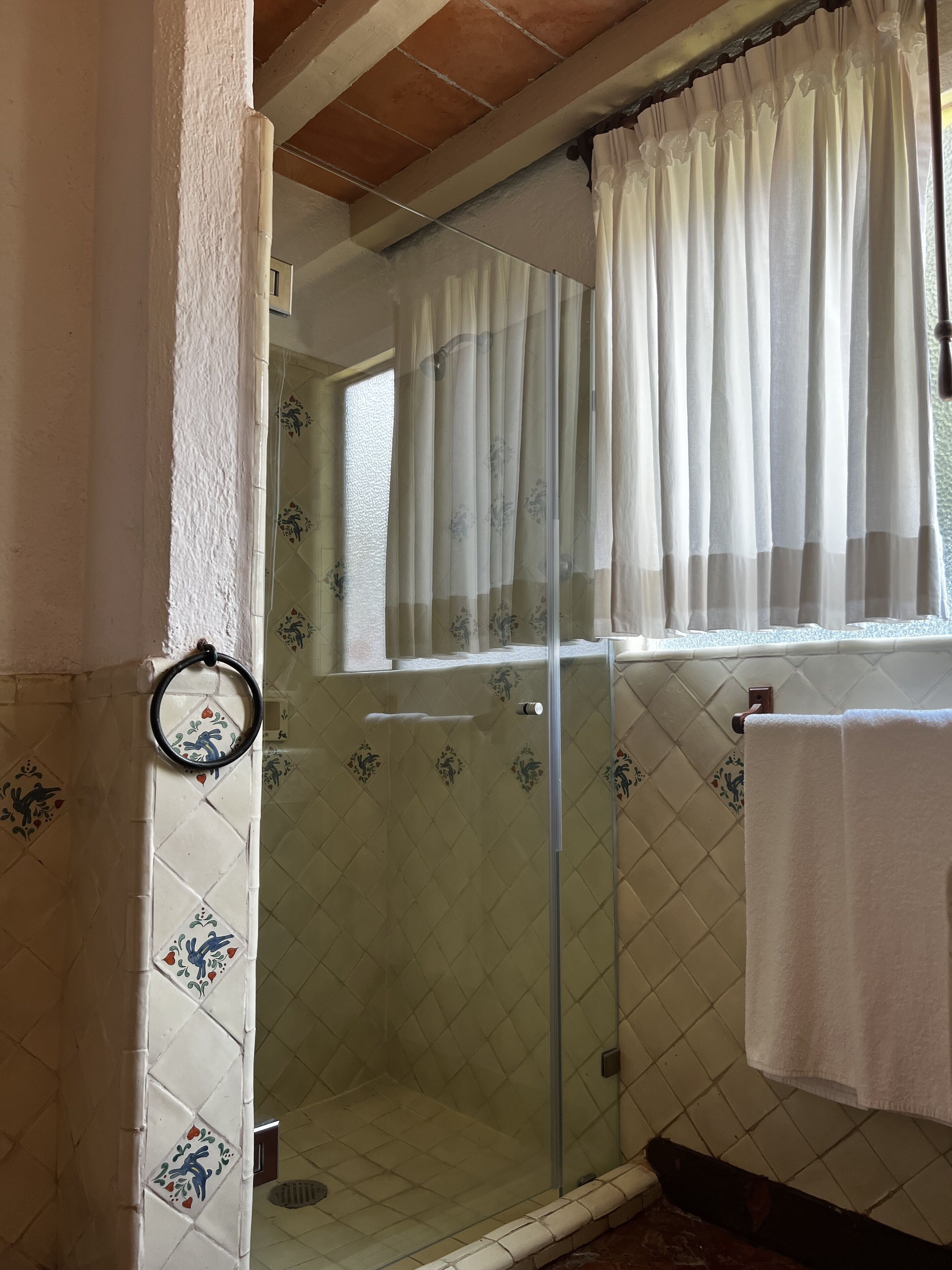 Un baño con cabina de ducha de vidrio, una ventana con cortina y una toalla colgada en un perchero.