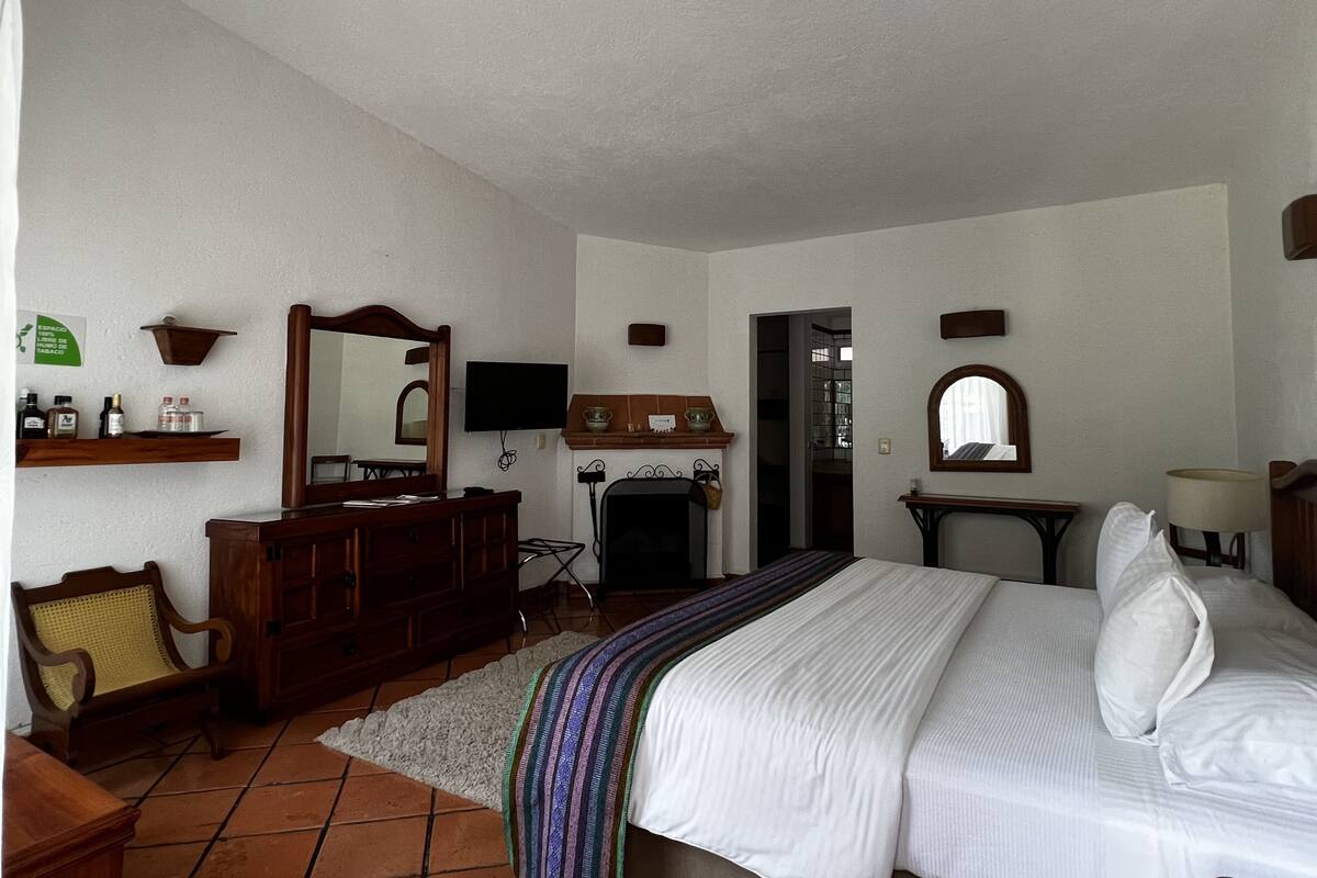 Un dormitorio con cama, cómoda, espejo, televisor y chimenea.