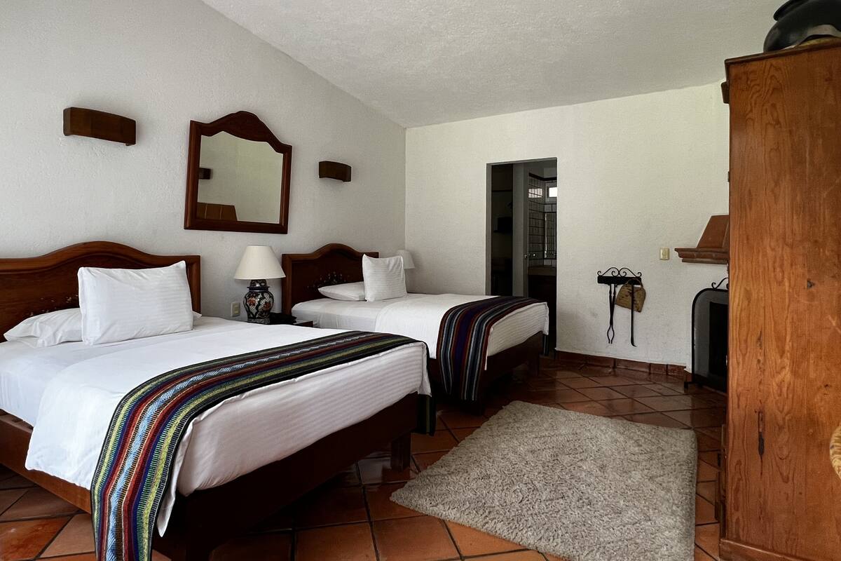 Una habitación de hotel con dos camas individuales, un armario de madera, un espejo y suelo de baldosas.