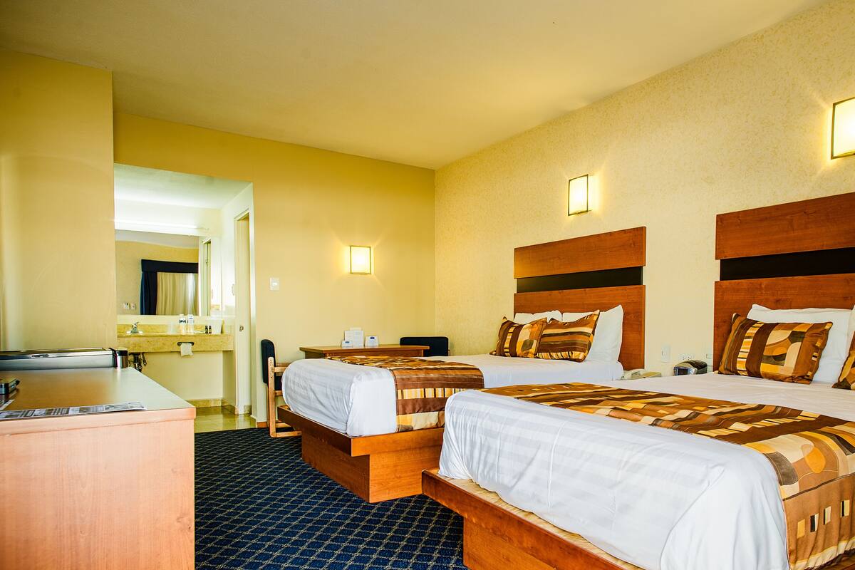 A hotel room with two beds, a desk, a mirror, and a bathroom visible through an open door.