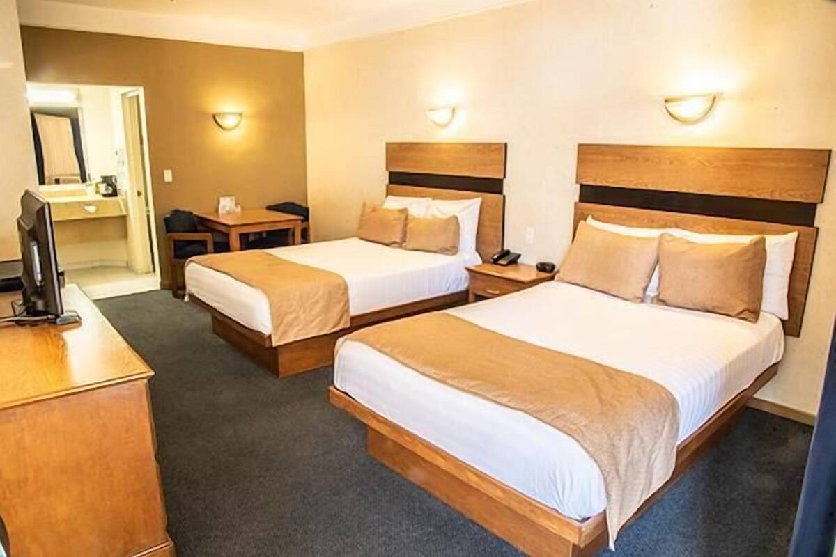 A hotel room with two beds, a desk, a chair, a TV, and a bathroom.
