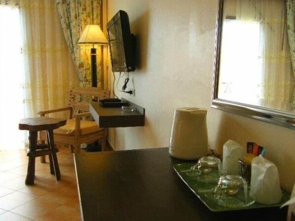 Una habitación pequeña con escritorio, silla, lámpara, televisor y ventana con cortinas.
