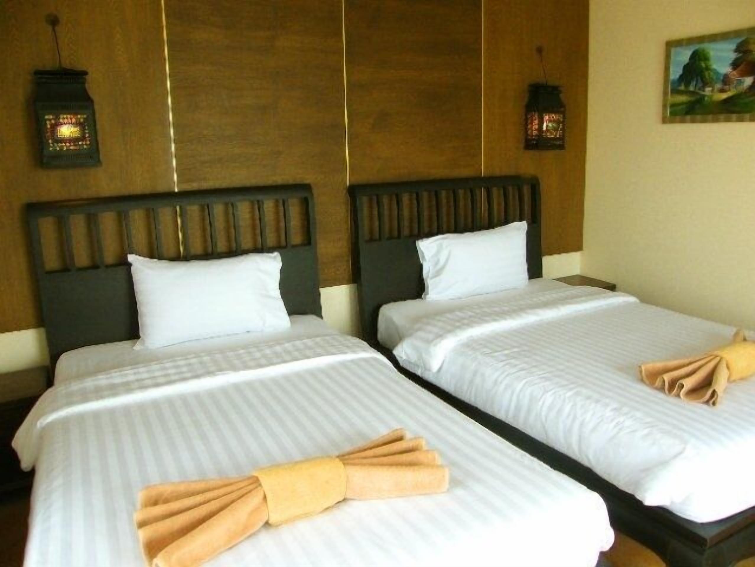 A hotel room with two beds, wooden headboards, white linens, and two wall-mounted lanterns.