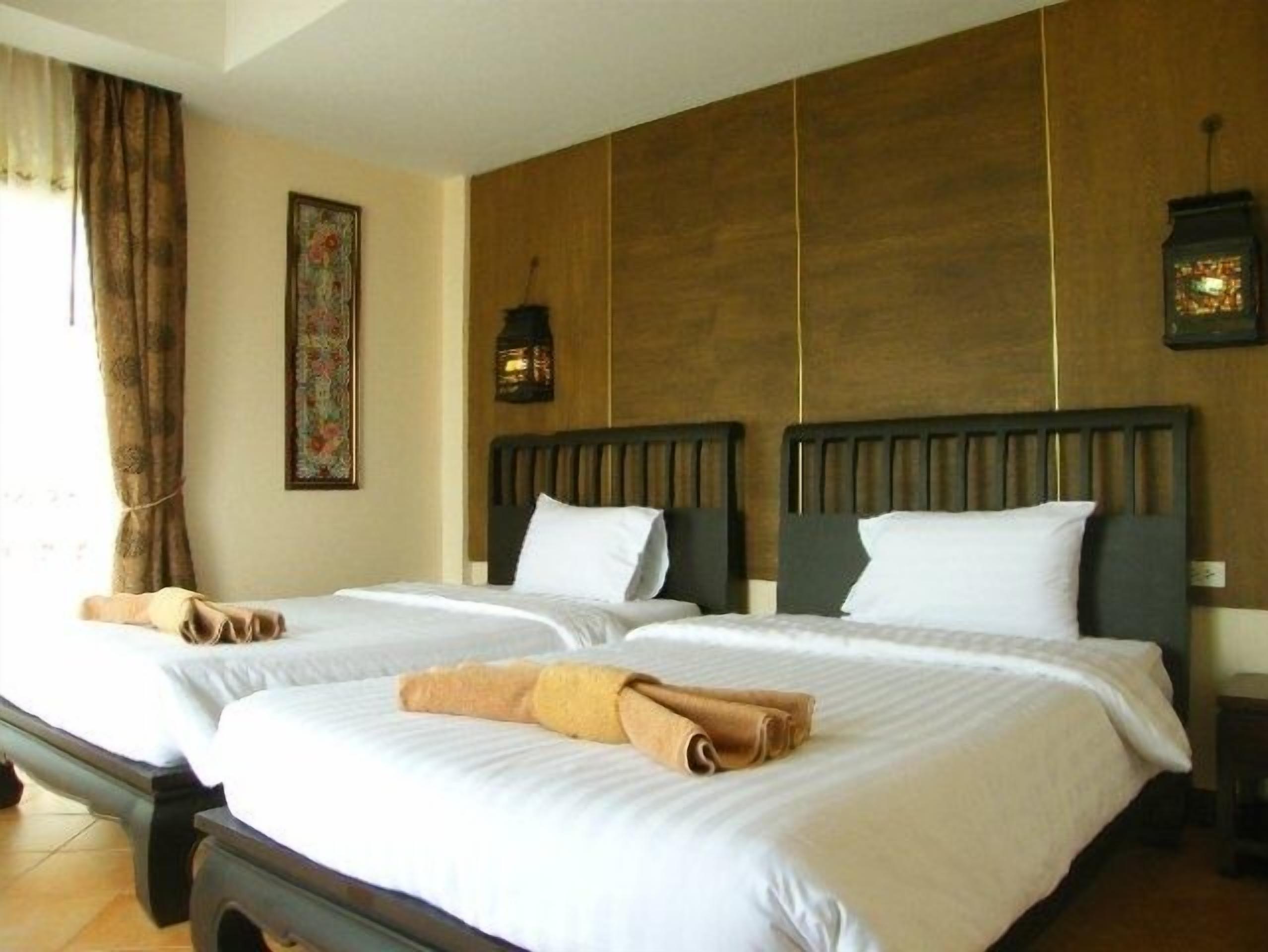 A hotel room with two beds, a wooden wall panel, a painting, and a nightstand with a lamp.