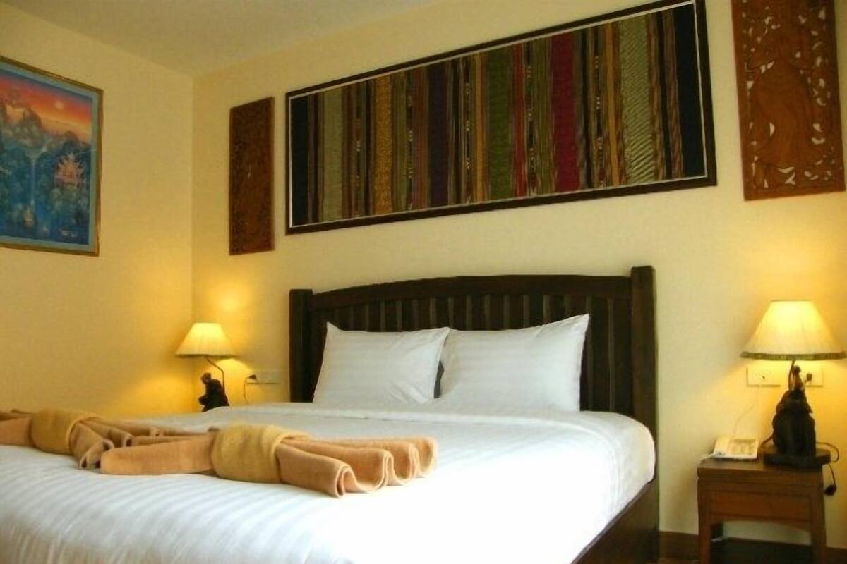 A neatly made bed with white linens and a brown blanket, two bedside lamps, a wooden nightstand, and a colorful striped artwork above the bed.