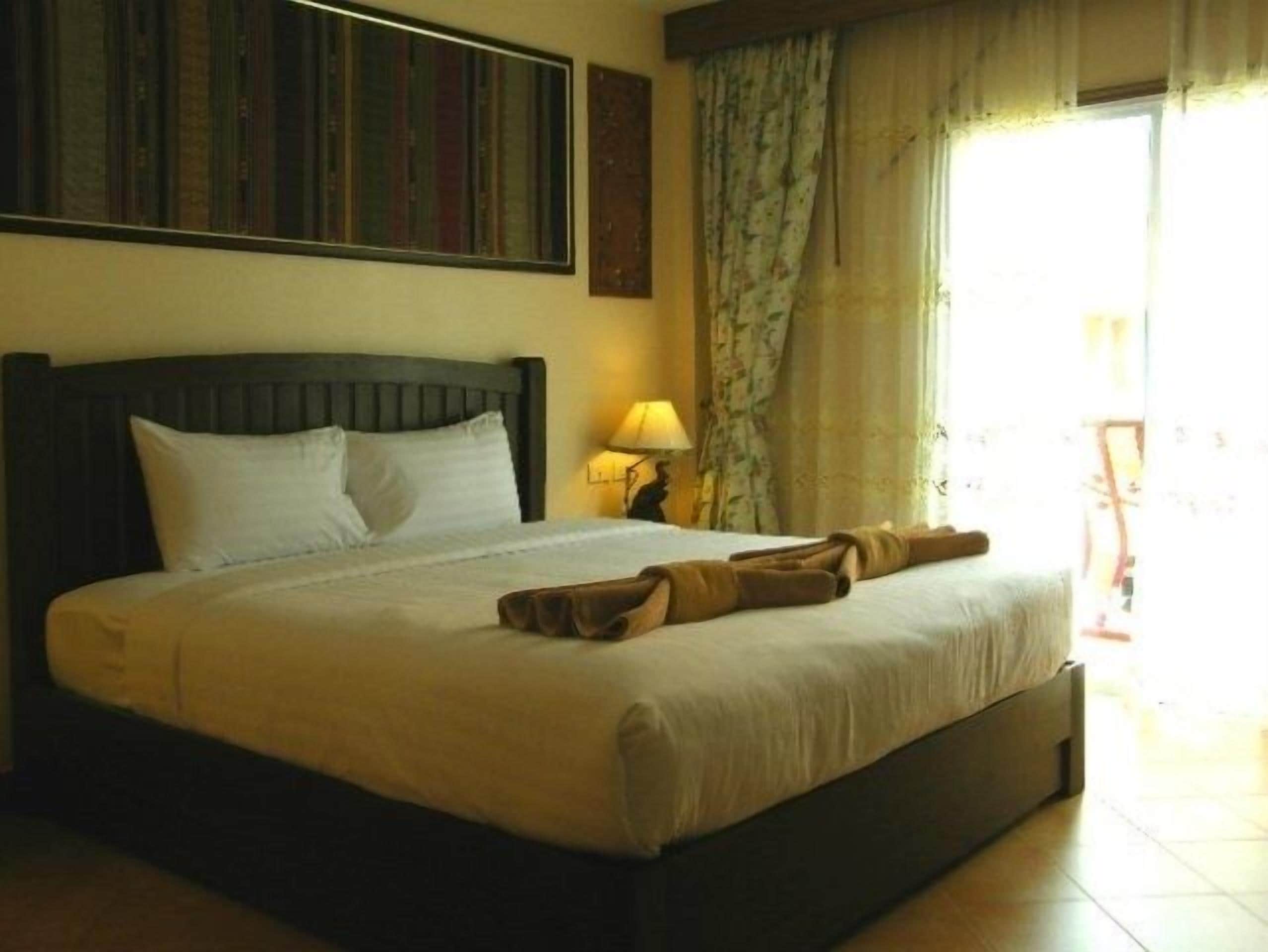 A neatly made bed with a dark headboard, a bedside lamp, and a window with curtains.