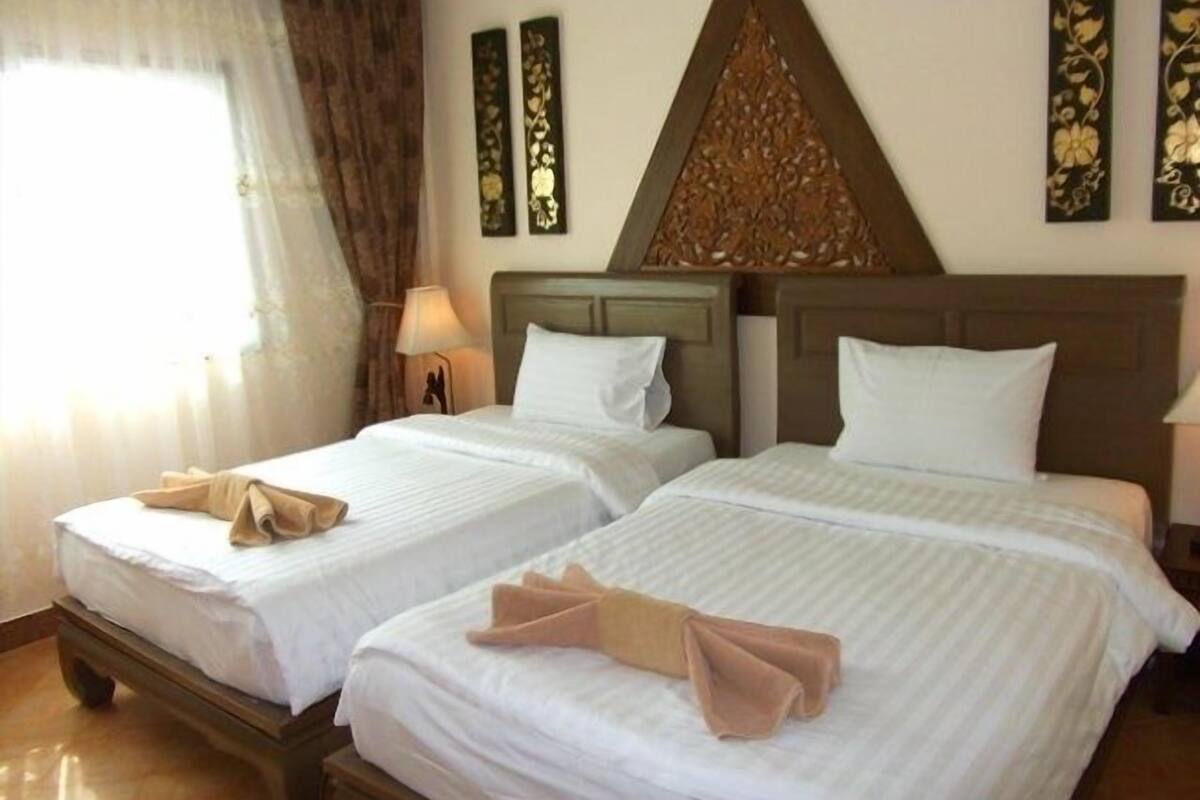A hotel room with two beds, a window with curtains, and decorative wall panels.