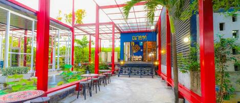 An outdoor cafe area with red structural elements, tables, and chairs.