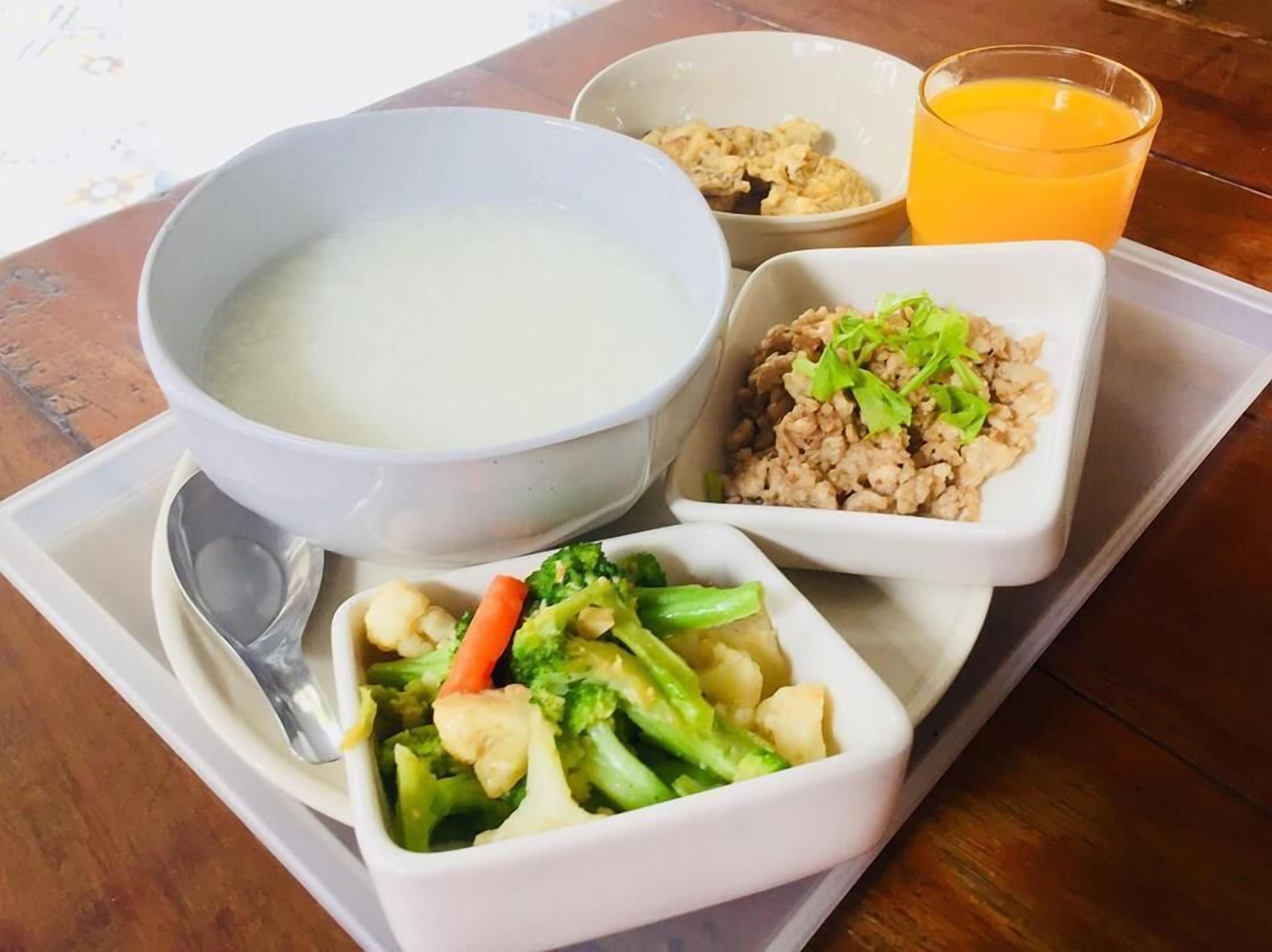 A tray with a bowl of soup, a bowl of rice with vegetables, a bowl of mixed vegetables, and a glass of orange juice.