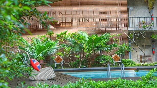 A poolside area with two lounge chairs, one with a red and blue pillow, and a wooden deck. - NY TH Hotel (Si Racha)