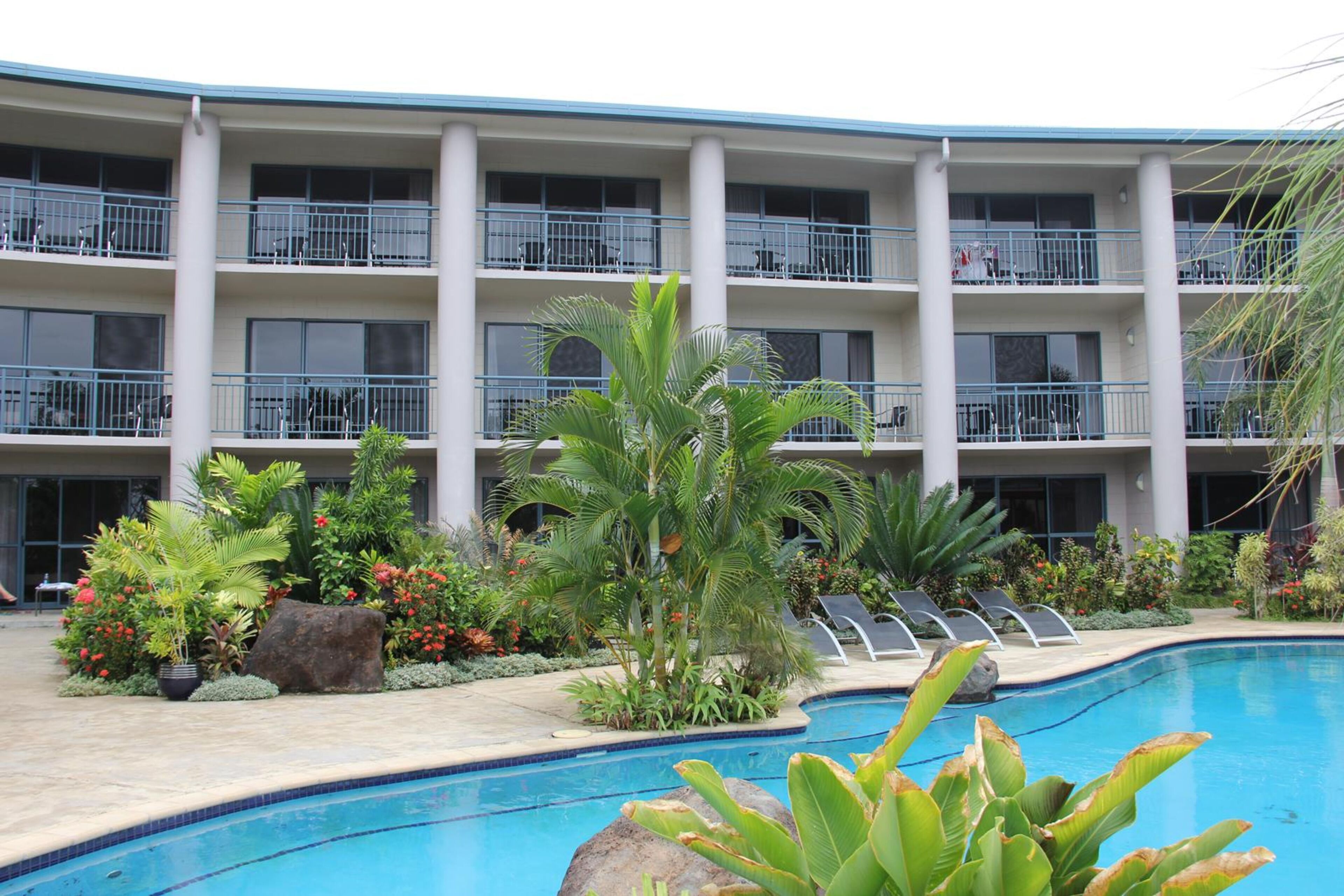 A hotel with a pool area, multiple balconies, and lush landscaping.