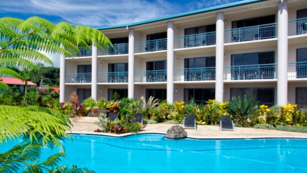 Un hotel con piscina rodeado de plantas tropicales y un edificio de varios pisos con balcones.