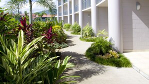Un pasillo de hotel con varios balcones, rodeado de abundante vegetación y palmeras.