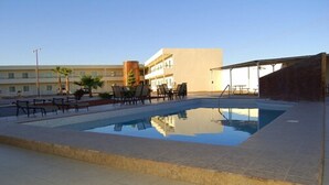A swimming pool with lounge chairs and a covered seating area, surrounded by buildings. - American Inn Hotel & Suites Delicias (Delicias)