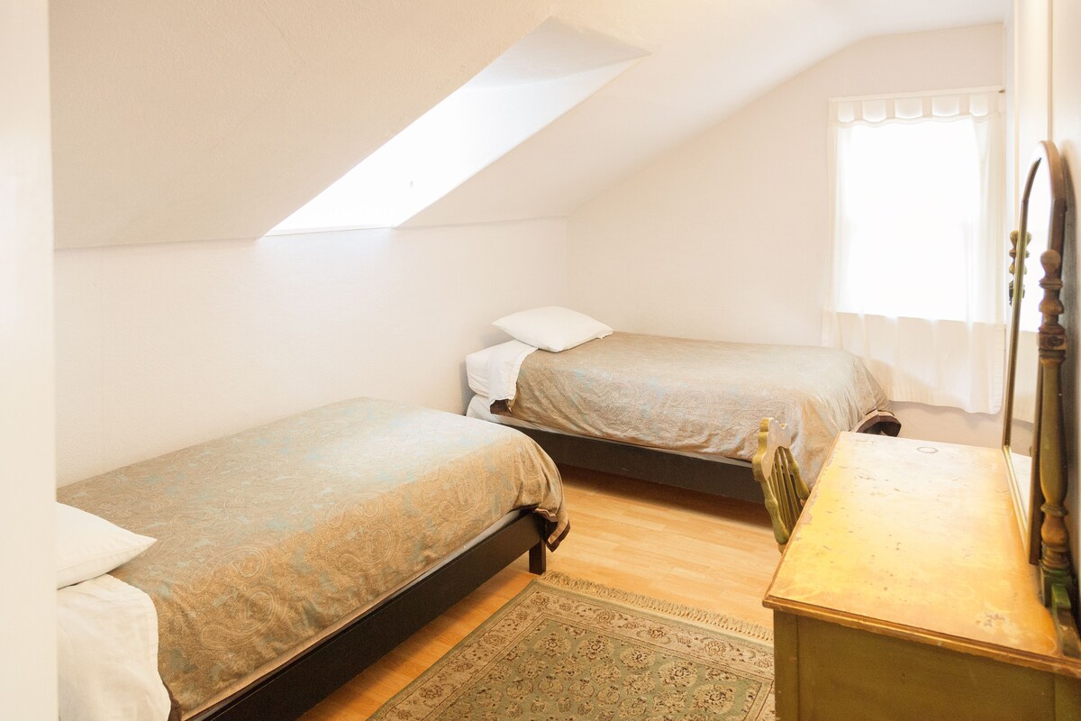 Ein kleines, gut beleuchtetes Schlafzimmer mit zwei Einzelbetten, einer Holzkommode und einem Oberlicht.