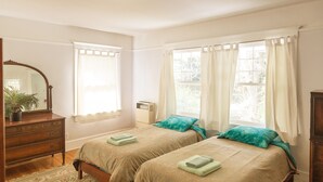Ein Schlafzimmer mit zwei Betten, einem Schminktisch, einem Spiegel und einem Fenster mit Vorhängen.