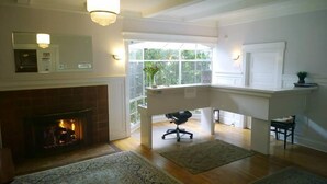 Ein geräumiges Wohnzimmer mit Kamin, hoher Decke und Blick ins Freie durch große Fenster.