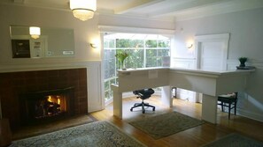 Ein geräumiges Wohnzimmer mit Kamin, hoher Decke und Blick ins Freie durch große Fenster.