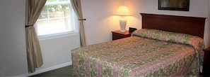 Une chambre à coucher avec un lit, une table de chevet, une lampe et une fenêtre avec des rideaux.