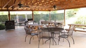 Un patio al aire libre con una mesa redonda y sillas, una parrilla y un ventilador de techo.