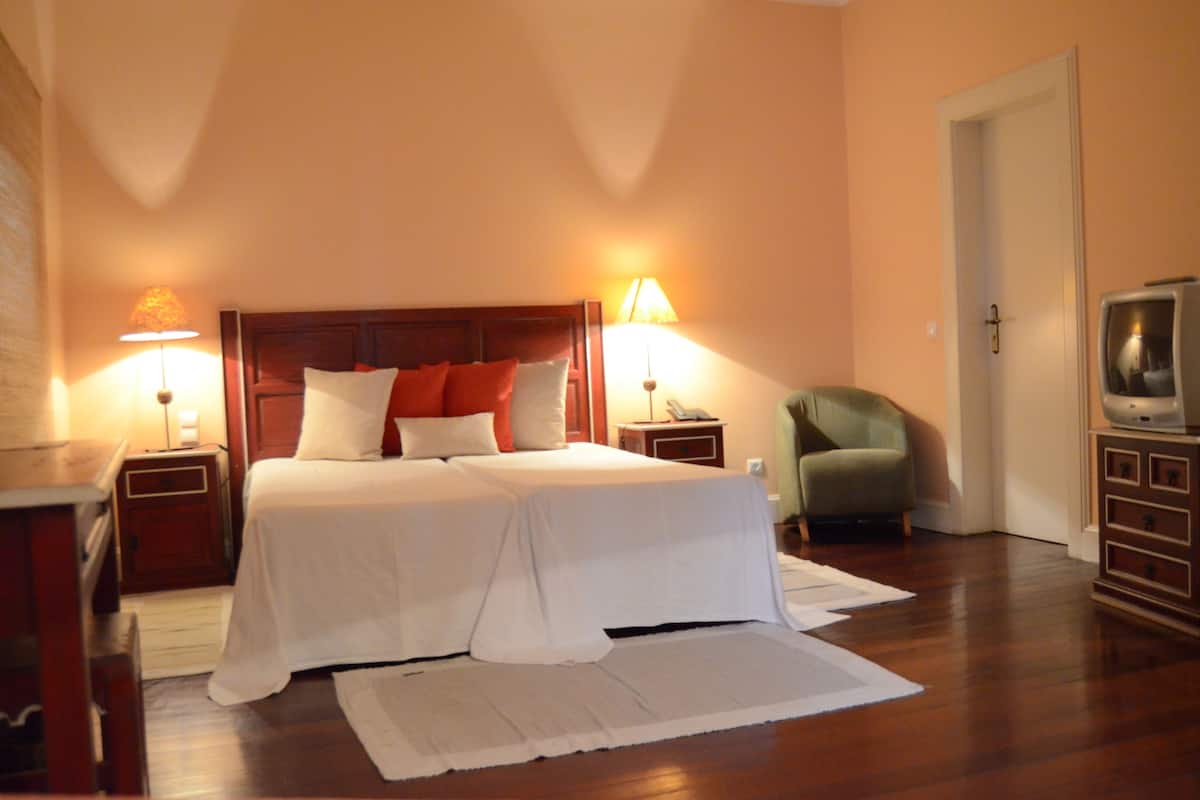 A hotel room with a double bed, two bedside lamps, a television, a chair, and a wooden dresser.